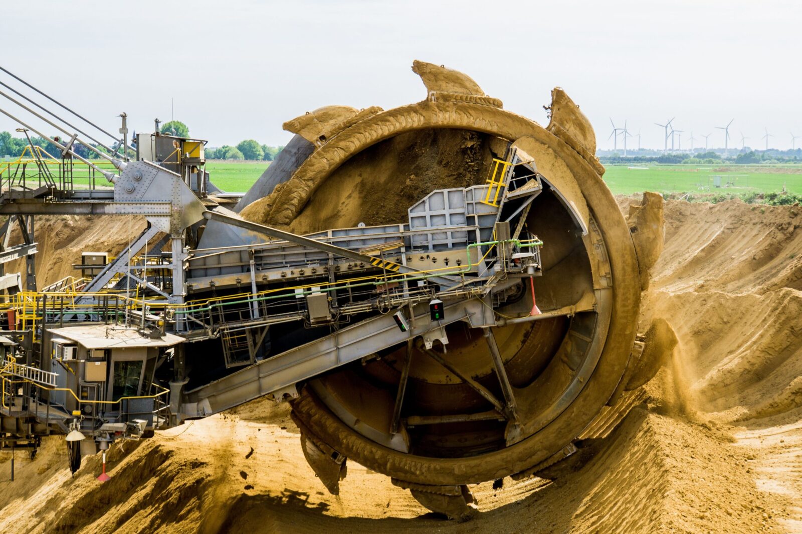 A large bucket wheel excavator working in an open pit mine against a green landscape.